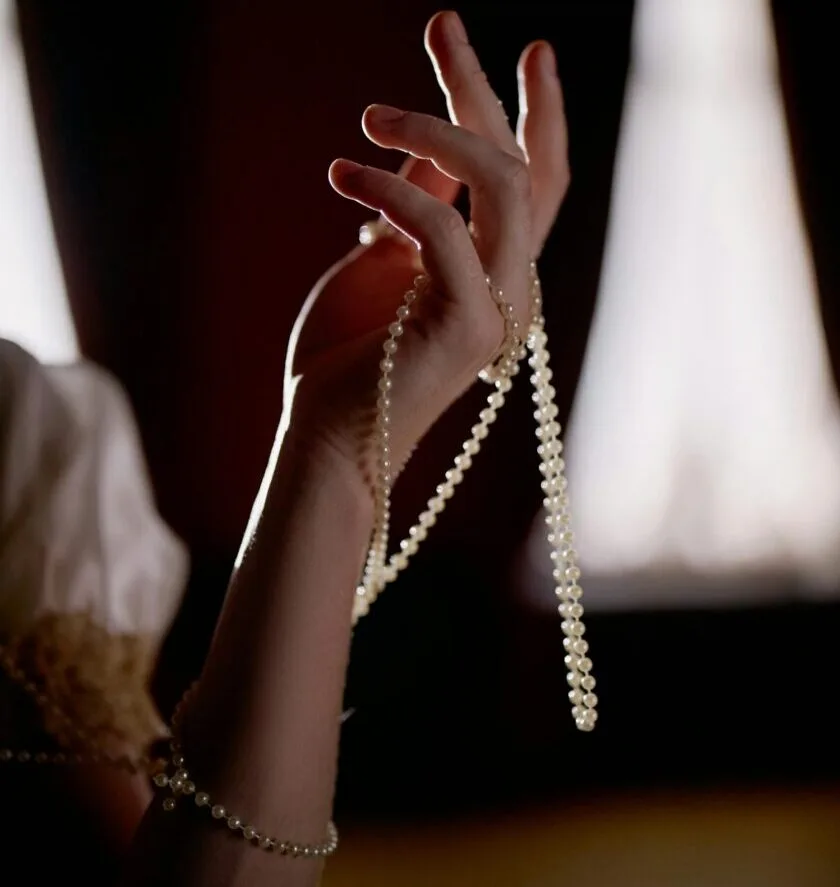 A close-up of a hand gracefully holding a pearl string in soft lighting.