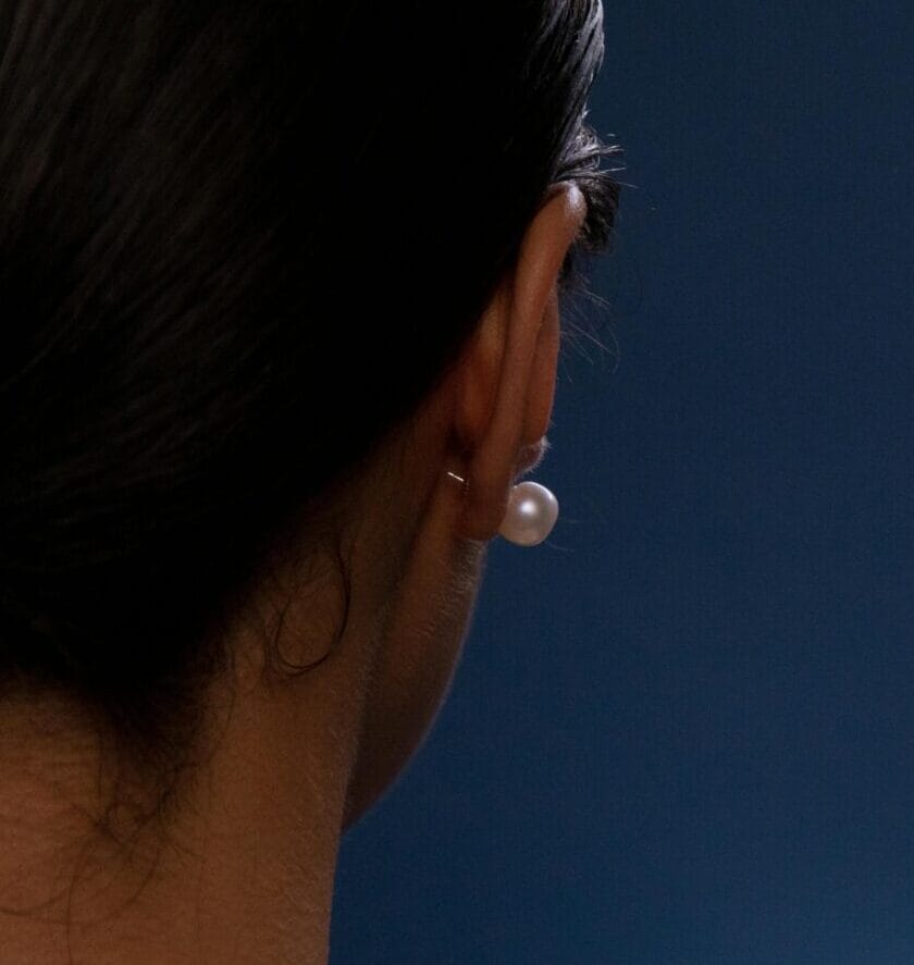 Close-up of a woman's bare shoulder adorned with pearl jewelry against a blue background.
